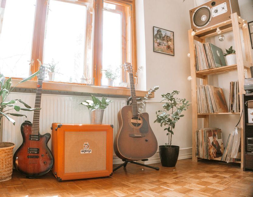 A cozy home studio corner with a guitar near a window.