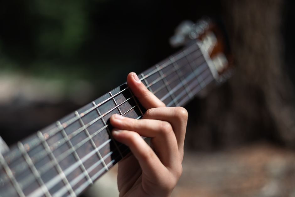 A hand forming a chord on an acoustic guitar fretboard.