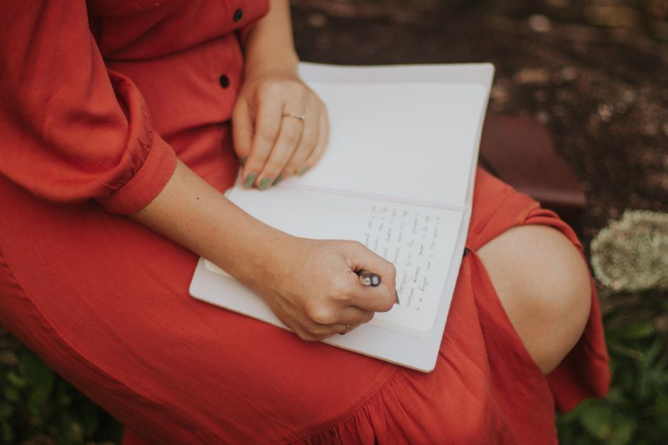 A hand writing in a lined notebook with a pen.
