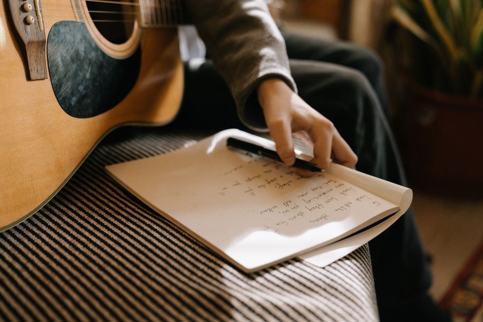 A songwriter's notebook and acoustic guitar on a wooden table, mid-session.